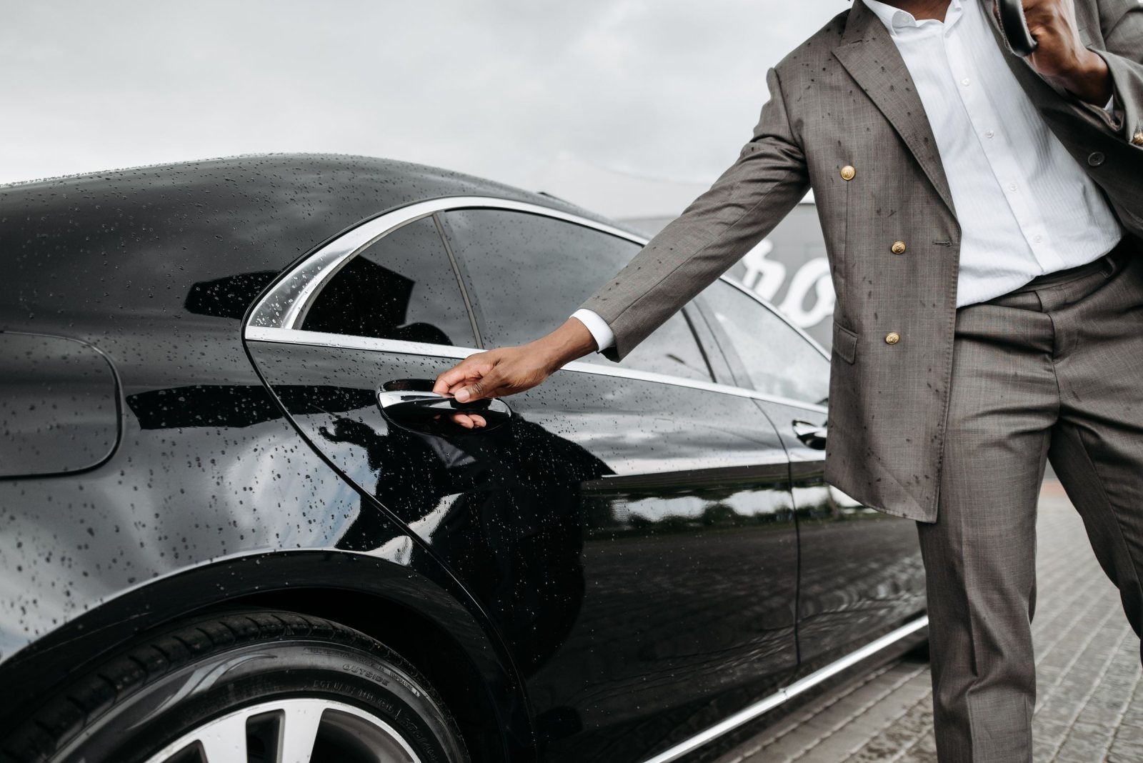 Chauffeur in a suit opening the rear door of a black sedan in the rain