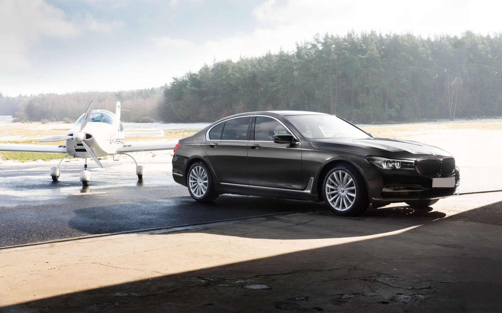 Black BMW 7 Series executive sedan parked beside a small airplane on an airfield
