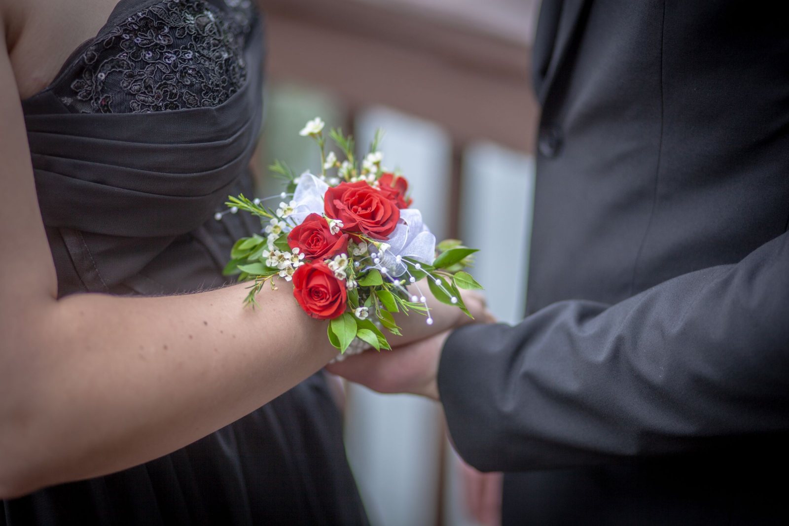 Red rose wrist corsage on a guest in a black formal dress, holding hands with a partner in a dark suit
