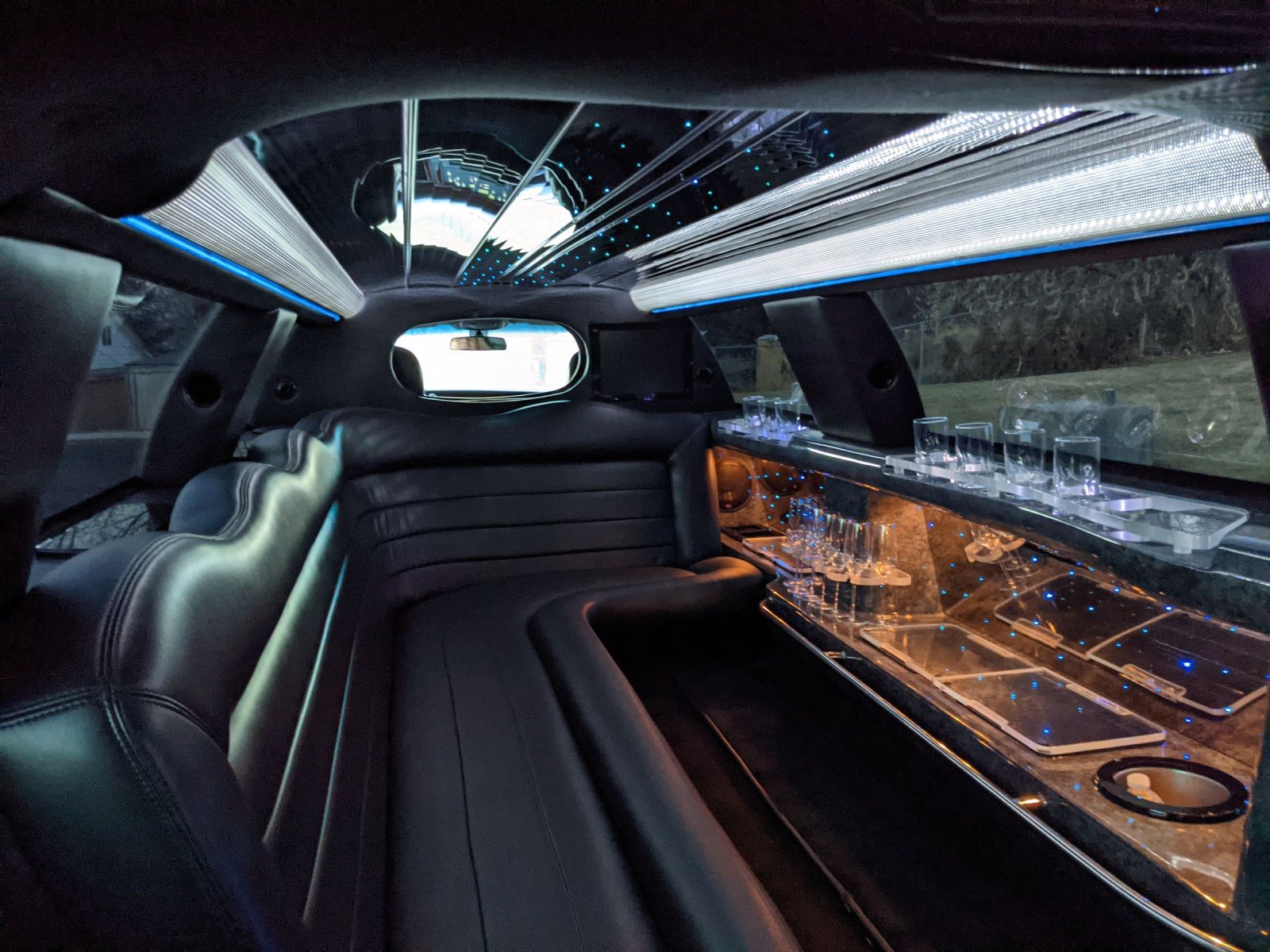 Inside a stretch limousine: black leather bench seating, a lit bar and ceiling lights