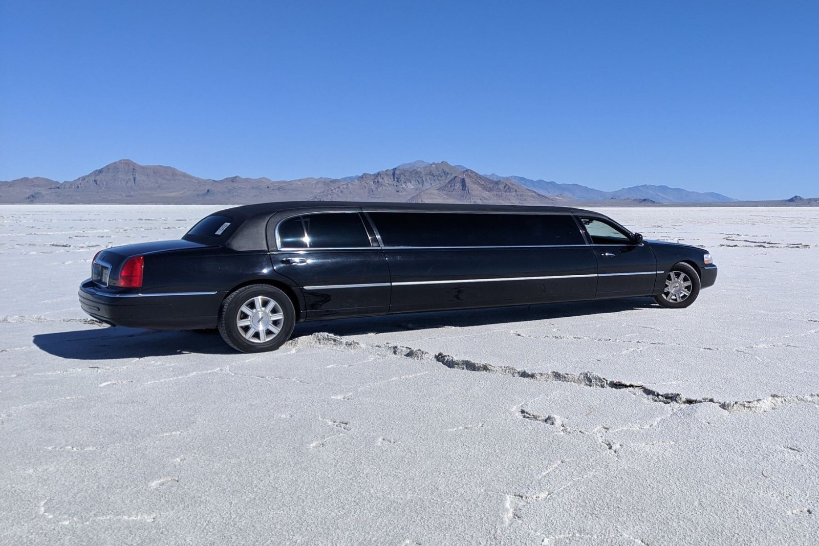 Black stretch limousine parked on a salt flat under a clear blue sky