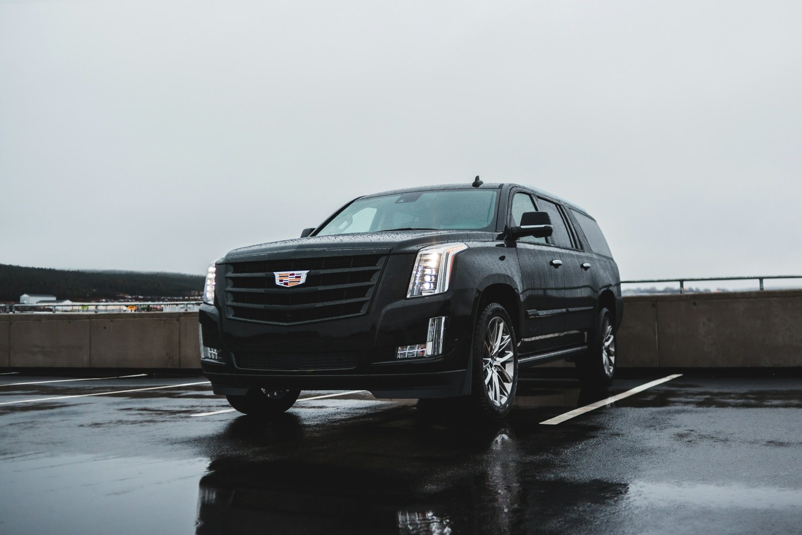 Black Cadillac Escalade ESV on a wet rooftop parking deck under a grey sky