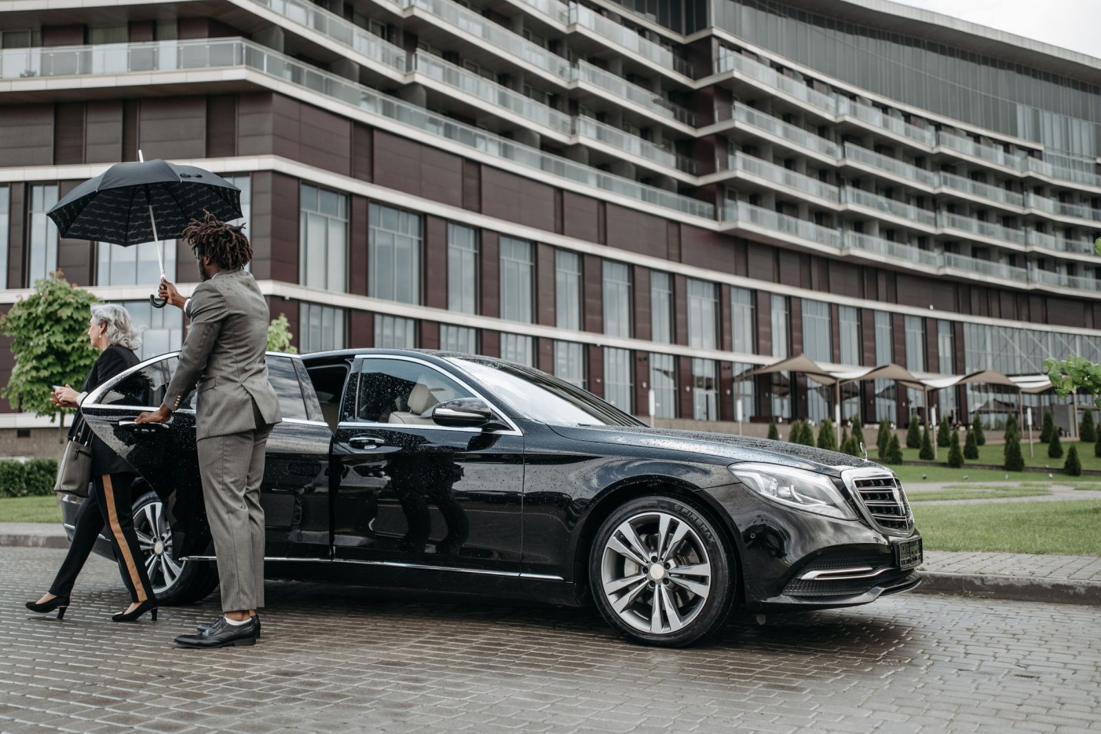 Chauffeur holding an umbrella and the door of a black Mercedes-Benz sedan for a passenger