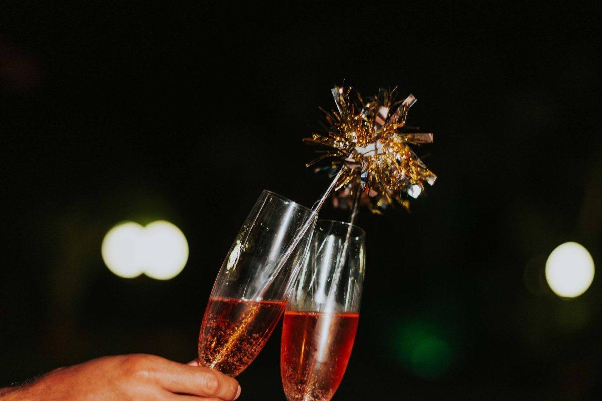 Two hands clinking glasses of pink champagne with a sparkler at night